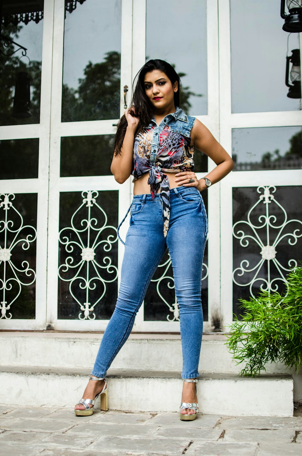 woman in blue denim jeans and white floral tank top leaning on white wooden door