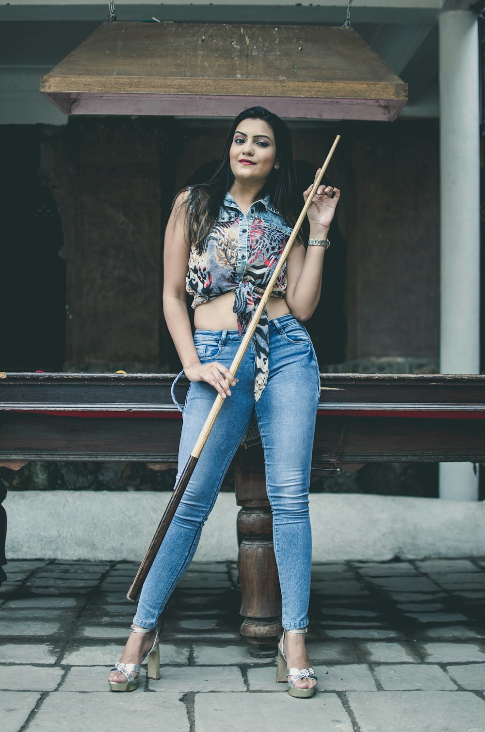 woman in white and red floral shirt and blue denim jeans holding brown wooden stick