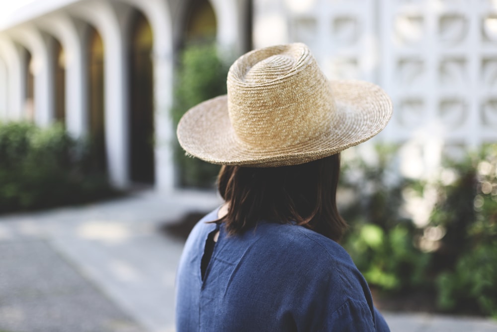 woman in blue shirt wearing brown straw hat standing on gray concrete road during daytime