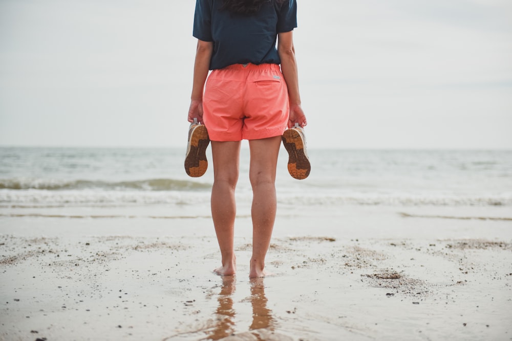 hombre con camisa azul y pantalones cortos naranjas de pie en la playa durante el día