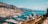 A coastal city with a bustling marina filled with numerous yachts and small boats. Tall buildings and hotels rise up along the shore, surrounded by mountainous terrain in the background. The ocean is calm and reflects the clear blue sky, creating a picturesque and luxurious atmosphere.