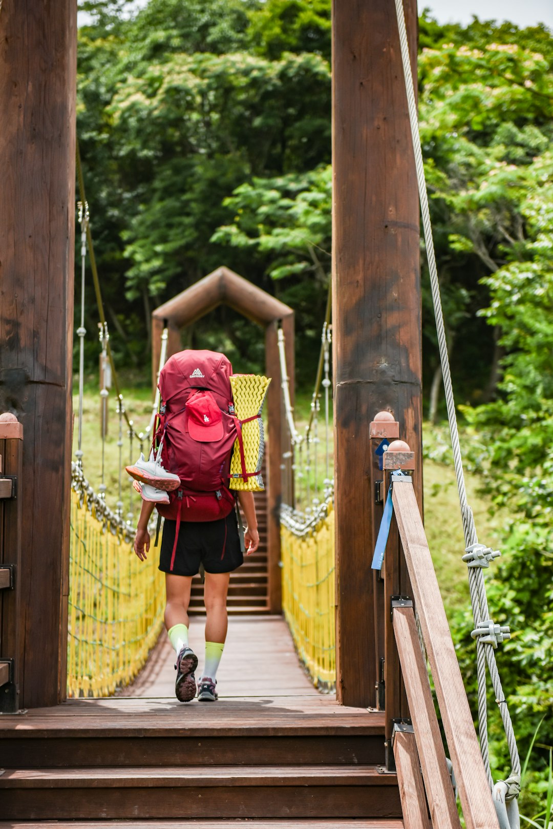 woman in red long sleeve shirt and black skirt walking on hanging bridge