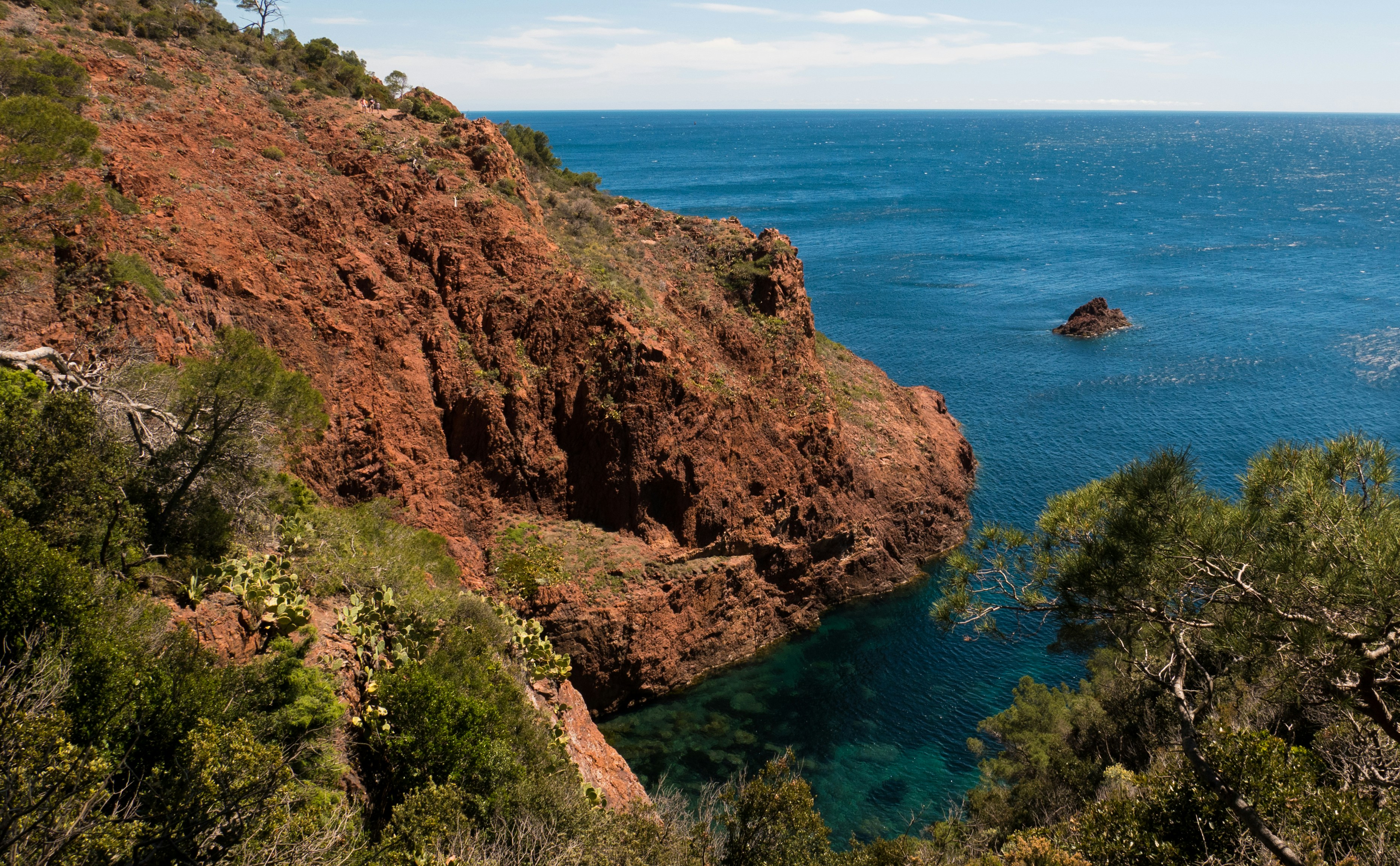 brown and green mountain beside blue sea under blue sky during daytime