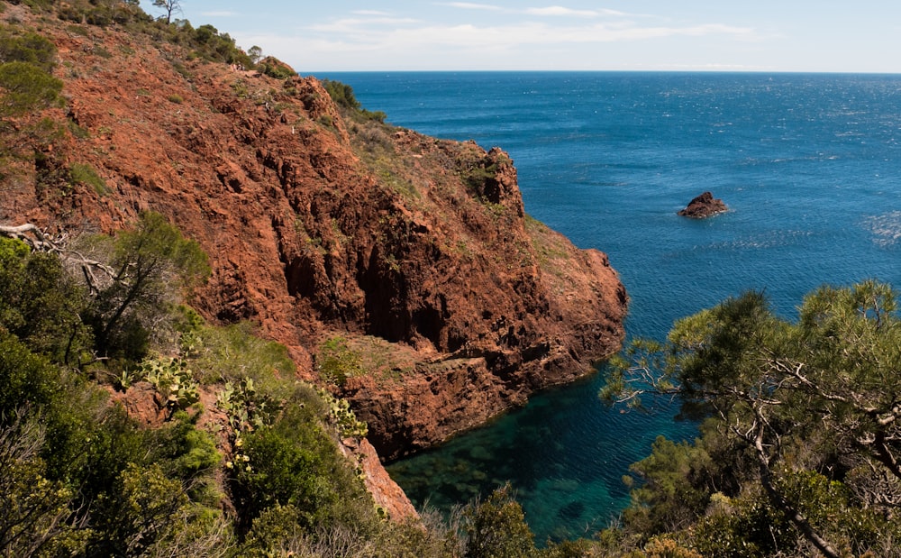 brown and green mountain beside blue sea under blue sky during daytime