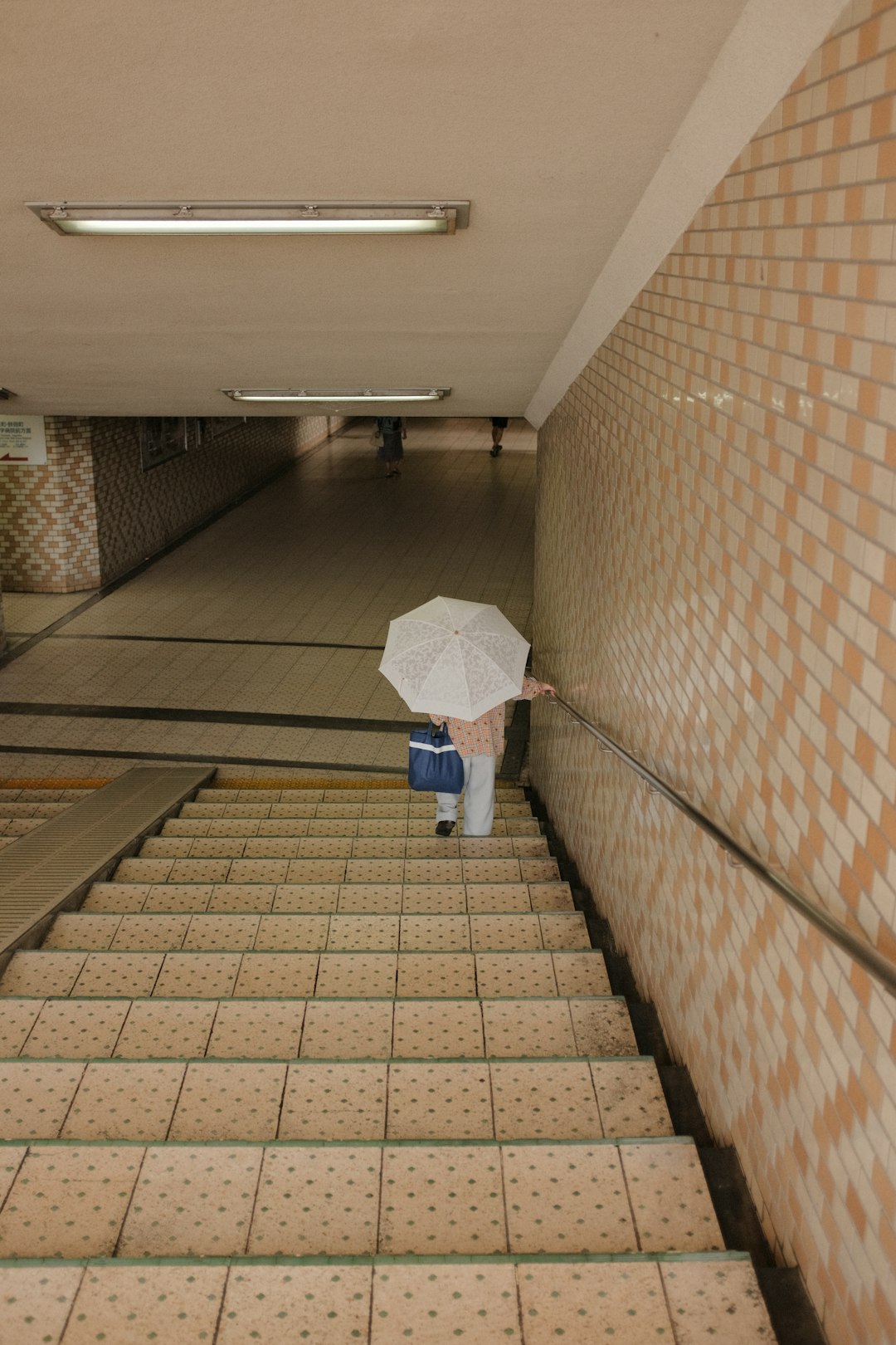 person in white shirt and blue denim jeans holding white umbrella walking on brown brick floor