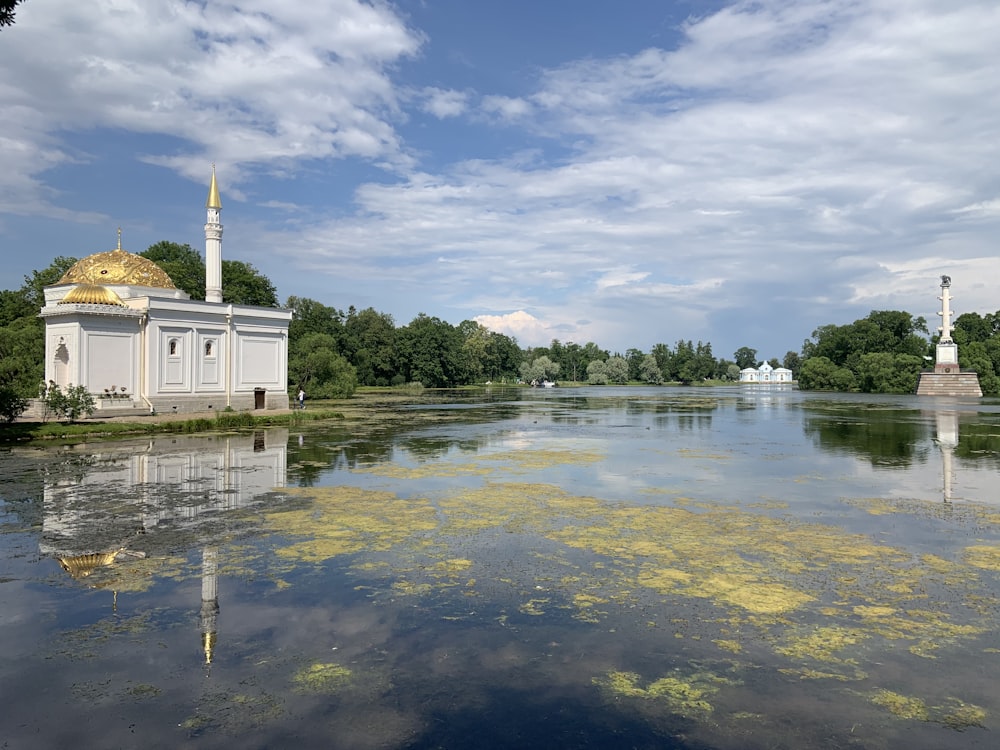 white concrete building near green trees and body of water under blue sky and white clouds