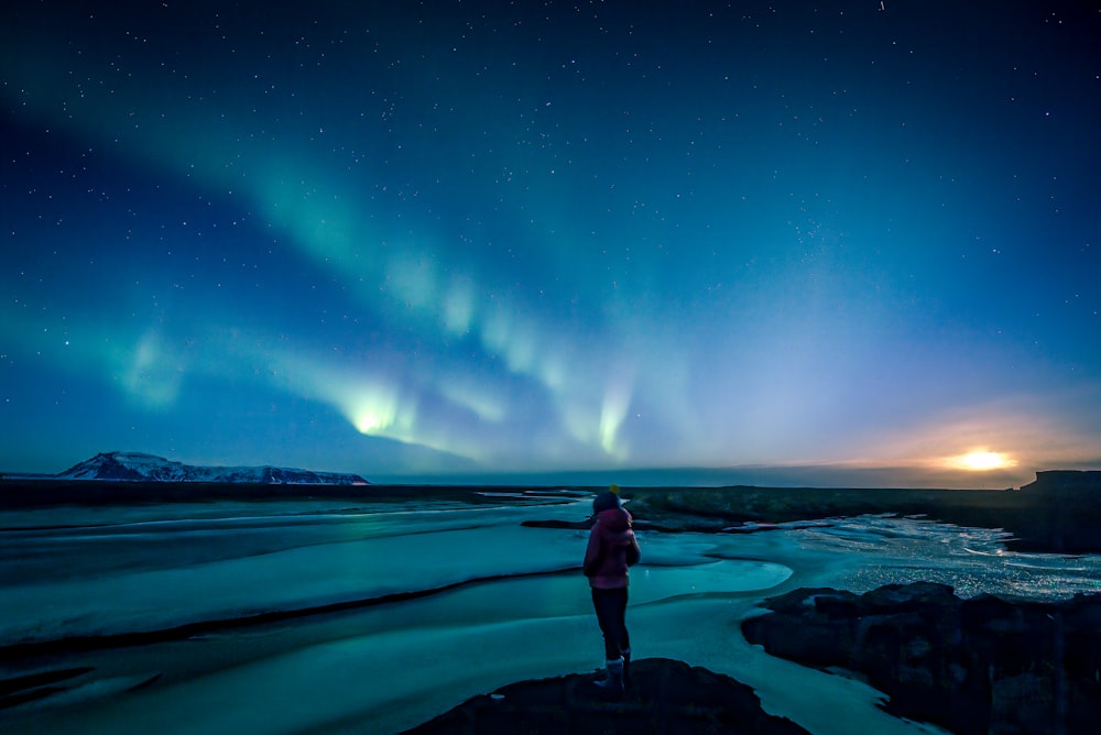 man standing on rock formation under blue sky during night time