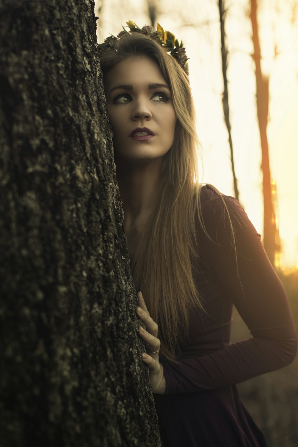 woman in brown long sleeve shirt leaning on brown tree during daytime
