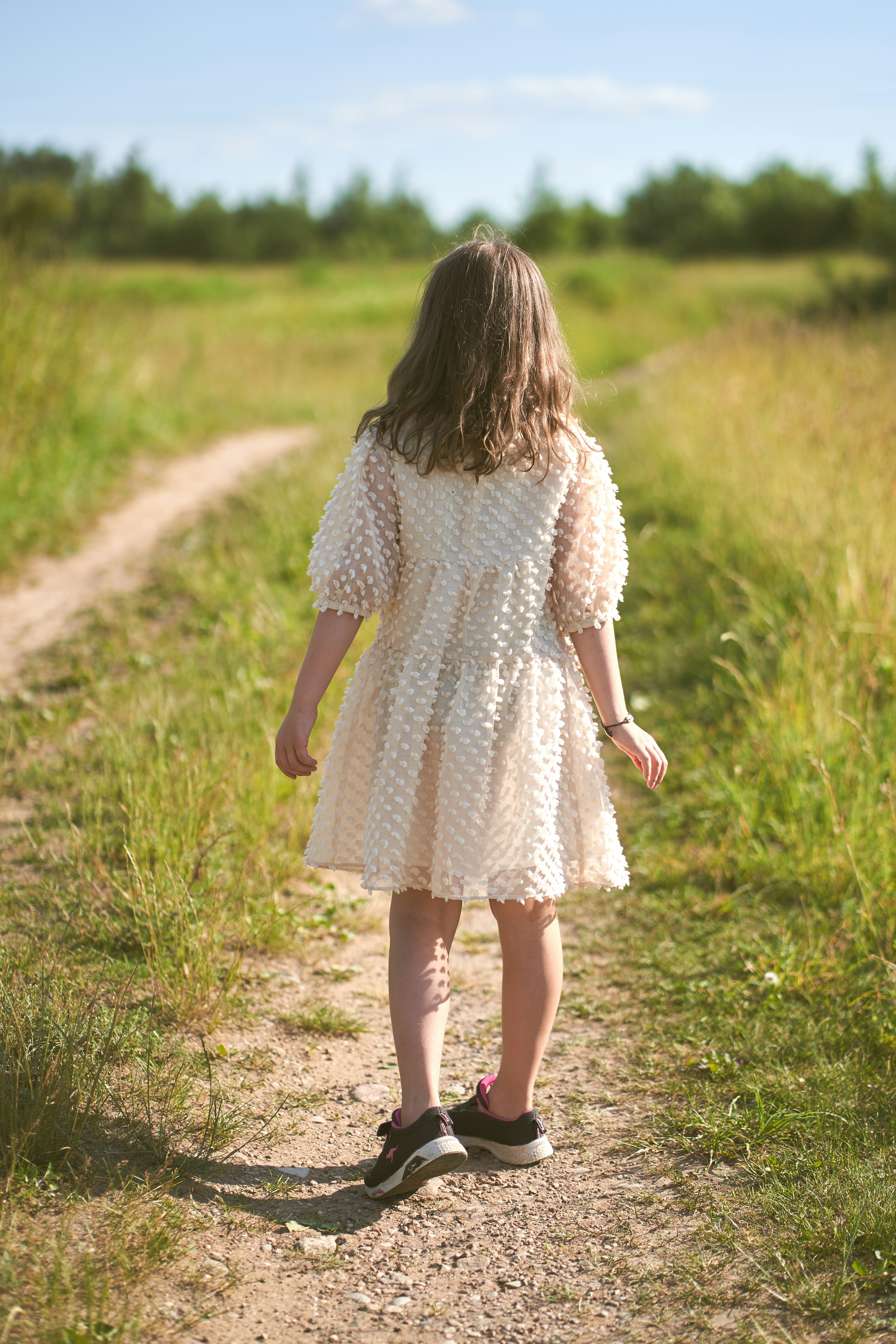 girl in white long sleeve dress walking on green grass field during daytime