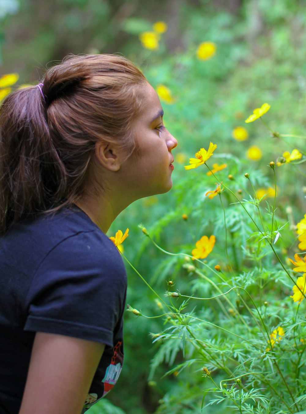 girl in blue crew neck t-shirt standing beside yellow flower during daytime