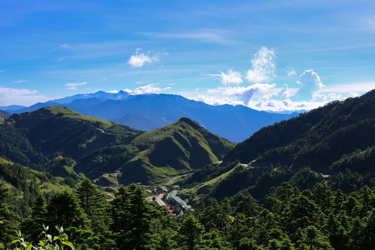 南投仁愛鄉山區的層層綠色山脈與藍天白雲，山谷間有幾棟建築