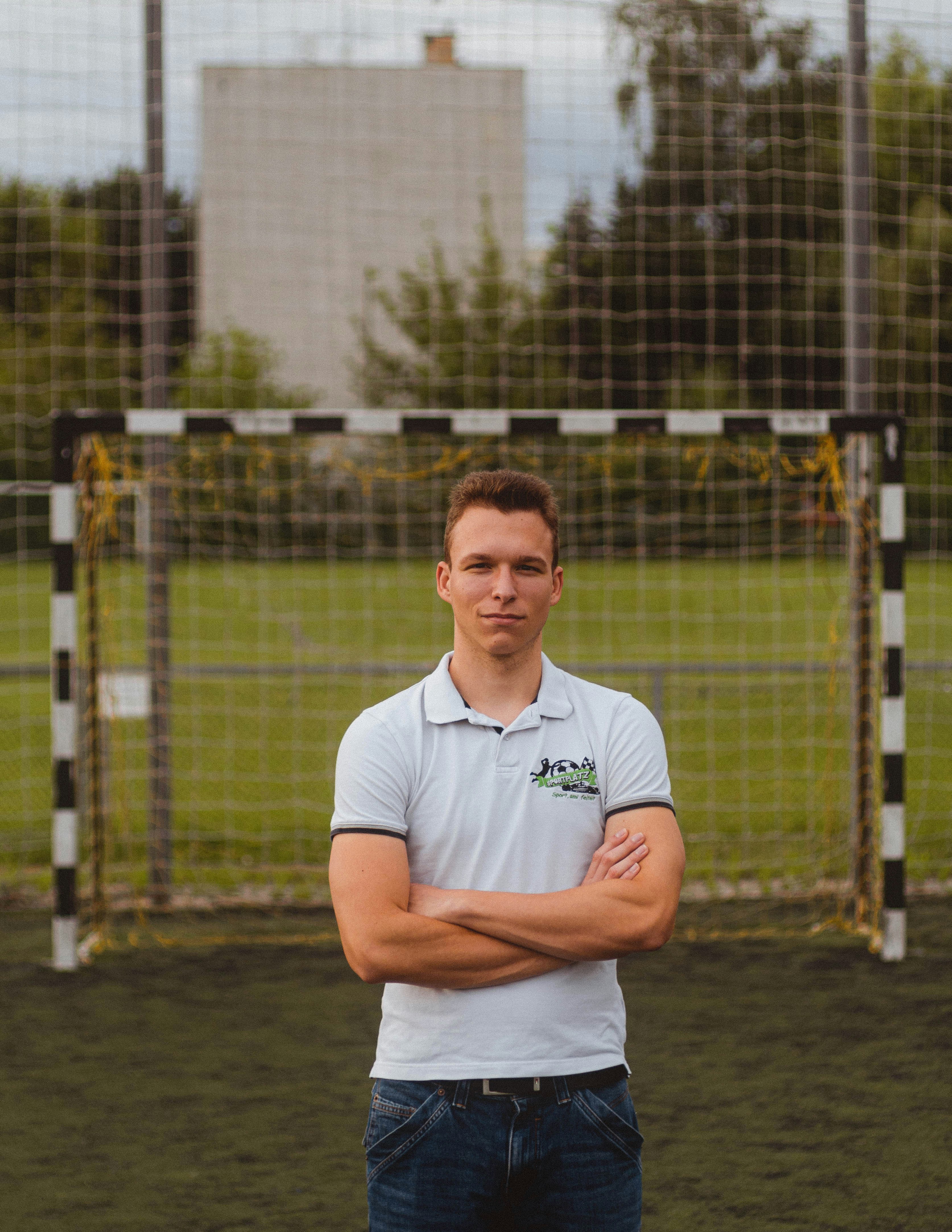 man in white polo shirt standing near fence during daytime