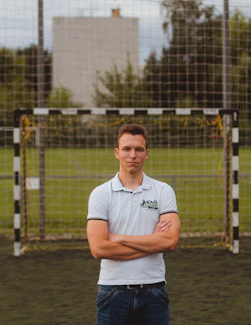 man in white polo shirt standing near fence during daytime