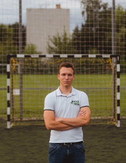man in white polo shirt standing near fence during daytime