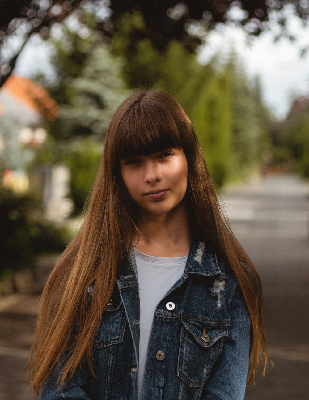 Frau in blauer Jeansjacke steht tagsüber in der Nähe von Bäumen