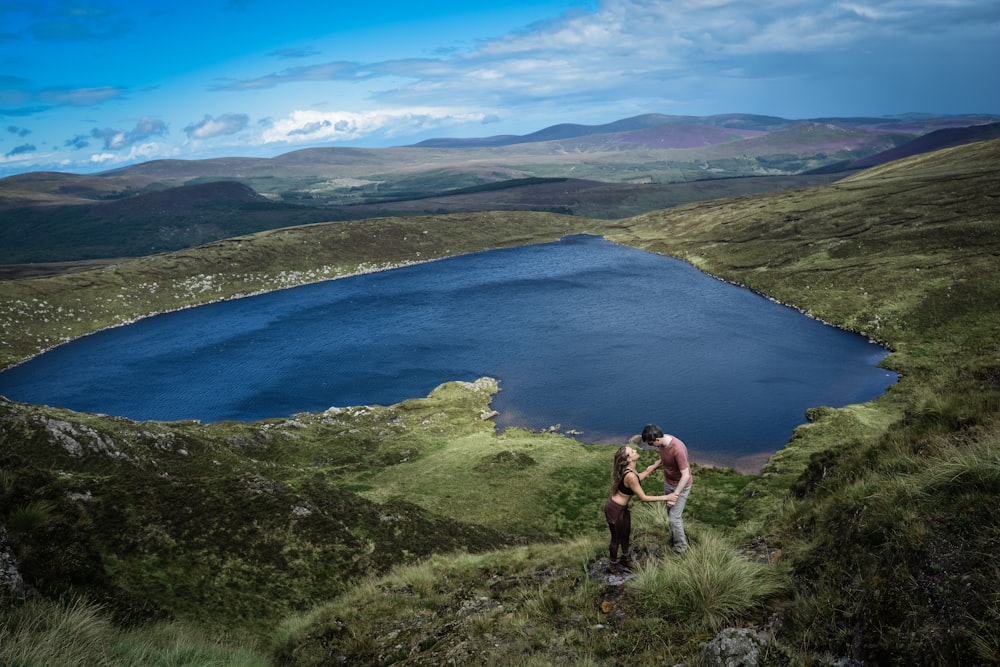 man in black shorts standing on cliff near lake during daytime