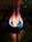 A close-up view of a lit gas stove burner with visible blue and orange flames. The stove grate is discernible in the background, casting shadowed lines on the stovetop surface.