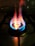A close-up view of a lit gas stove burner with visible blue and orange flames. The stove grate is discernible in the background, casting shadowed lines on the stovetop surface.