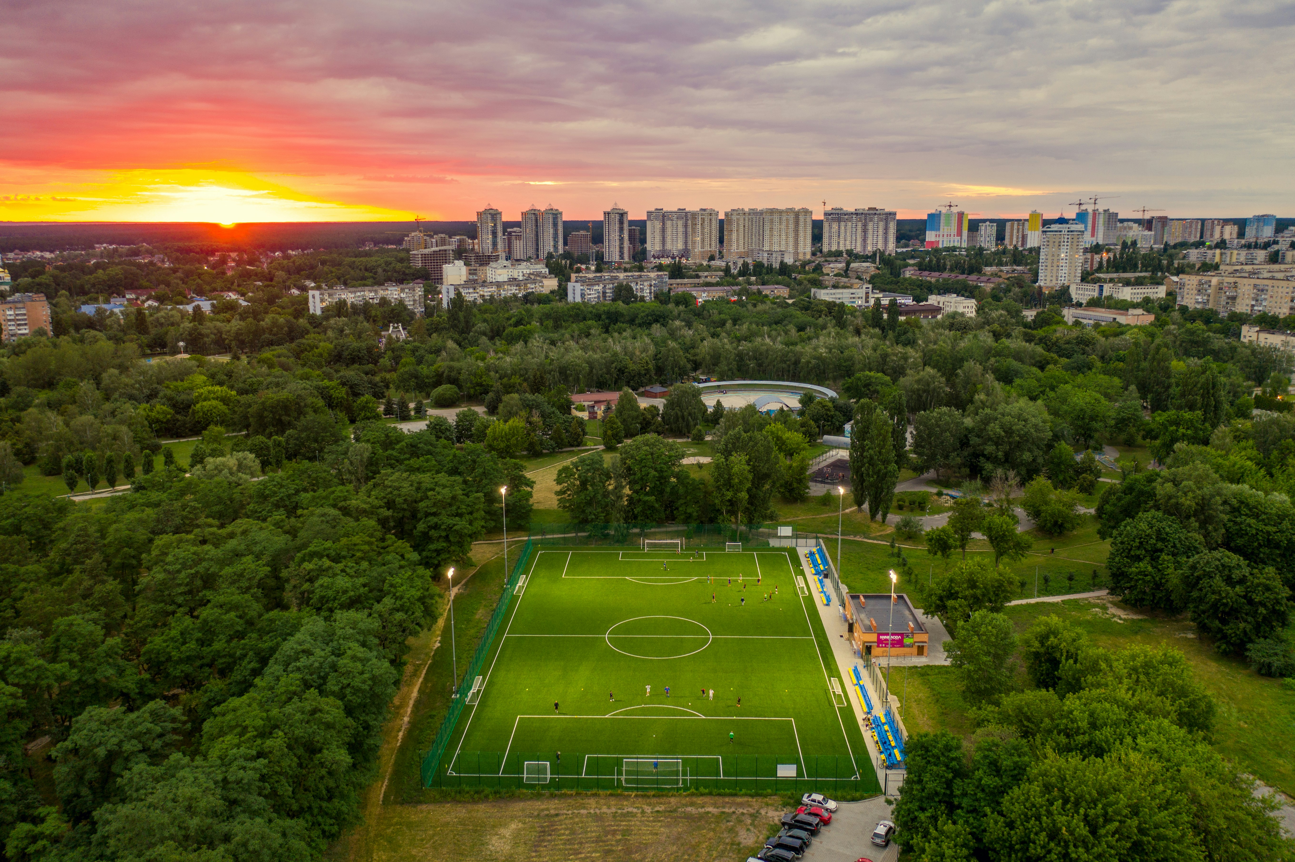 Wide-angle view of a floodlit soccer match at dusk, players in action, warm orange sky in background
