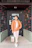 man in orange button up long sleeve shirt and black pants standing beside black wooden door