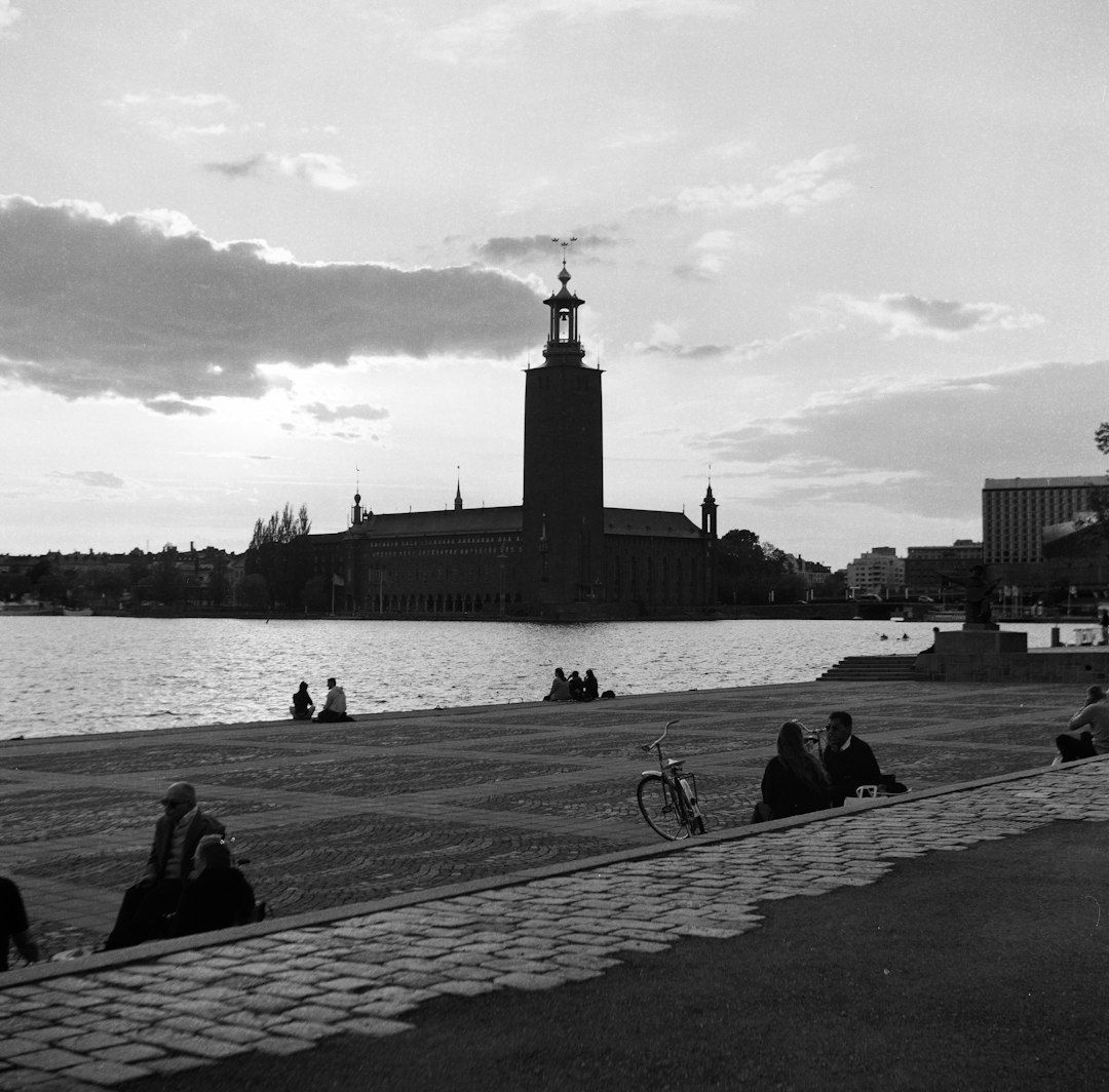 grayscale photo of man riding bicycle on road near body of water