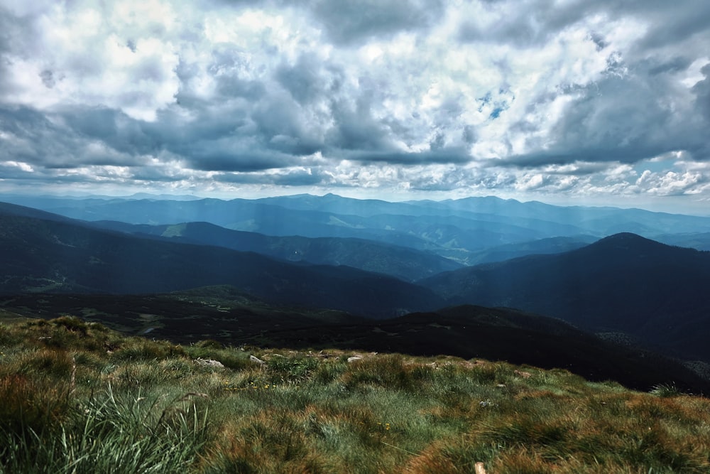 green grass field and mountains under white clouds