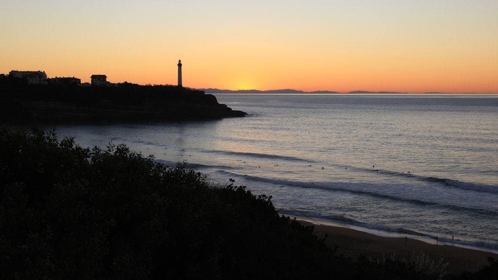 silhouette of lighthouse near body of water during sunset