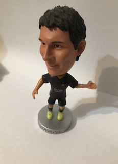 A bobblehead figure of a soccer player wearing a dark jersey with a logo and 'Qatar Airways' printed on it. The figure has short dark hair, light-colored shoes, and is mounted on a round base with the word 'soccerstarz'. The background is neutral, likely a plain surface.