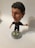 A bobblehead figure of a soccer player wearing a dark jersey with a logo and 'Qatar Airways' printed on it. The figure has short dark hair, light-colored shoes, and is mounted on a round base with the word 'soccerstarz'. The background is neutral, likely a plain surface.