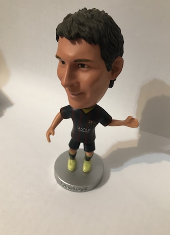 A bobblehead figure of a soccer player wearing a dark jersey with a logo and 'Qatar Airways' printed on it. The figure has short dark hair, light-colored shoes, and is mounted on a round base with the word 'soccerstarz'. The background is neutral, likely a plain surface.