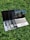 Multiple laptops are stacked on top of each other, placed on a grassy surface. The screen of the topmost laptop displays a reflection of a building and a railing.