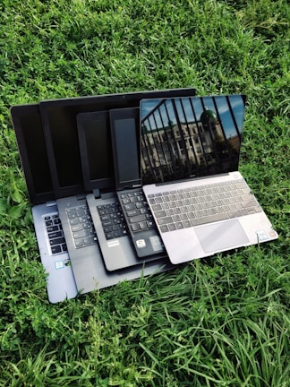 A stack of gently used laptops with pastel green accents ready for resale.