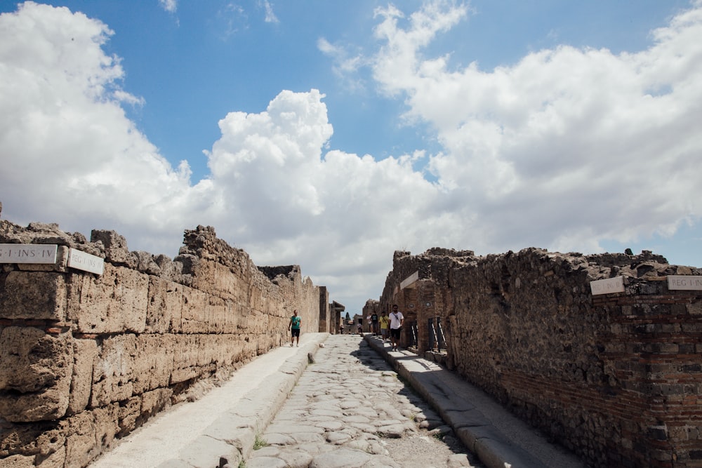 a cobblestone street lined with stone buildings under a cloudy blue sky