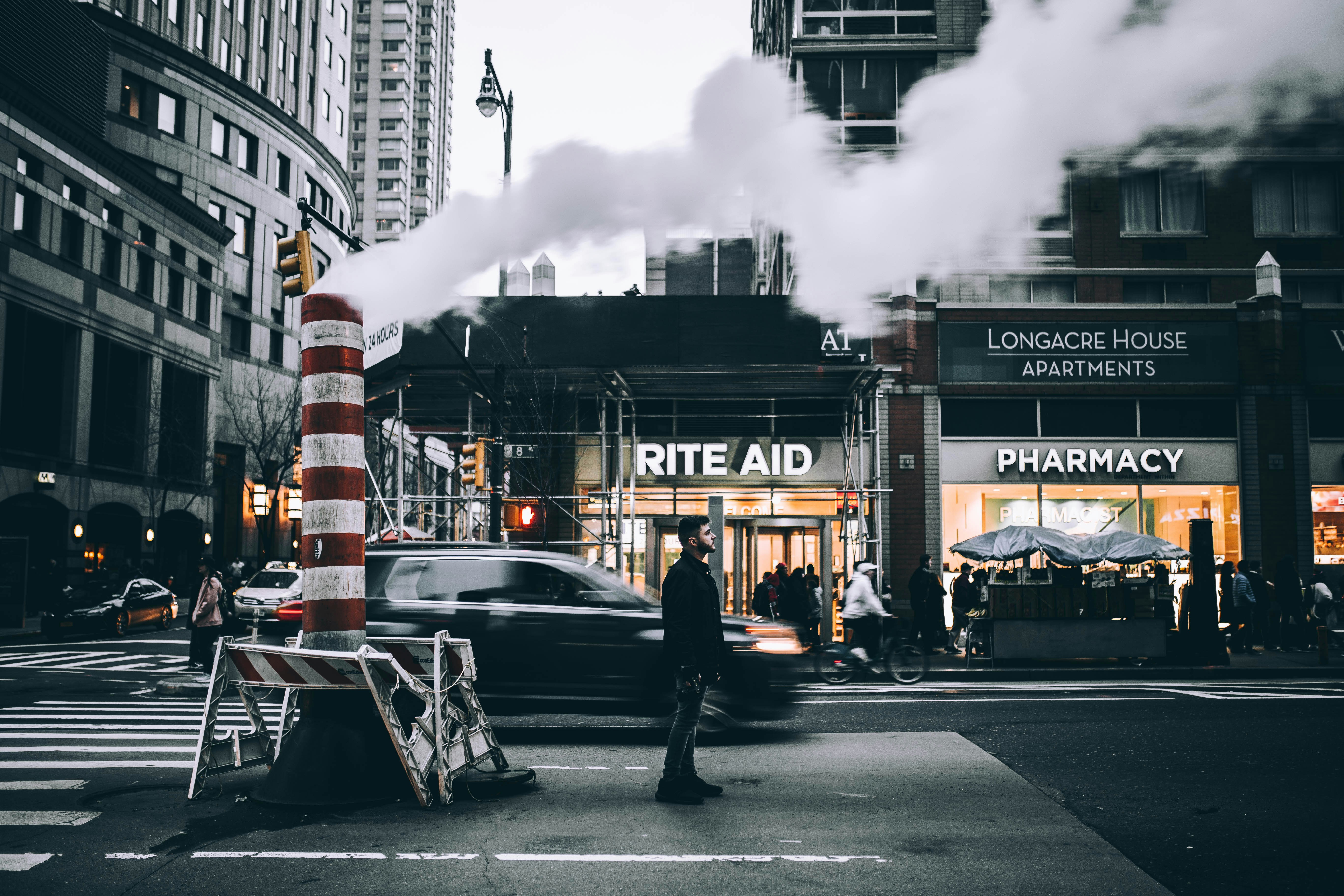 man in black jacket walking on street near white car during daytime