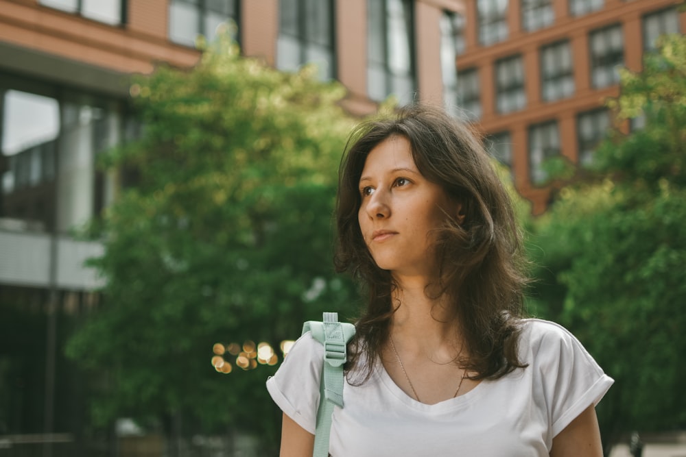 woman in white scoop neck shirt standing near green trees during daytime