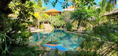 An inviting pool villa with lush greenery and a private pool reflecting the clear blue sky.