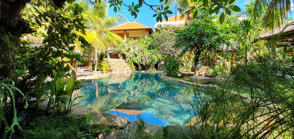 A serene villa poolside at sunset with lush tropical greenery surrounding the area.
