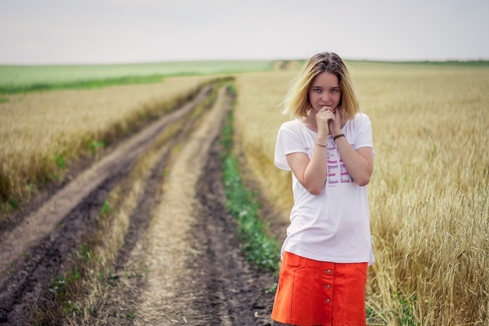 woman in white shirt and red skirt standing on pathway between green grass field during daytime