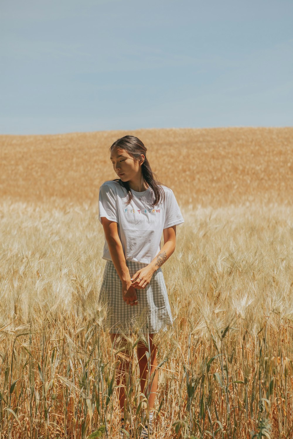 woman in white t-shirt and black and white plaid skirt standing on brown grass field
