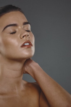 A person with closed eyes appears to be in a serene or contemplative state, with their head tilted slightly and hand resting on the neck. The skin has a smooth and glowing appearance.