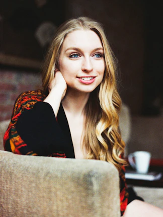 A playful woman with vibrant hair, laughing gently, sitting on a plush sofa.