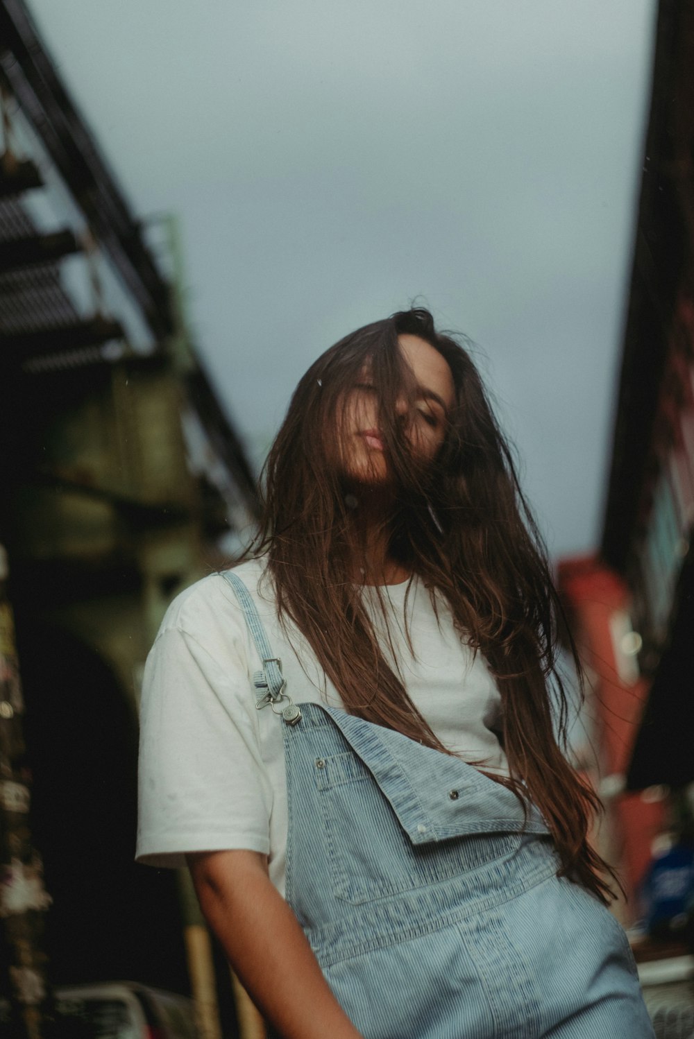 a woman with long hair wearing overalls and a white t - shirt