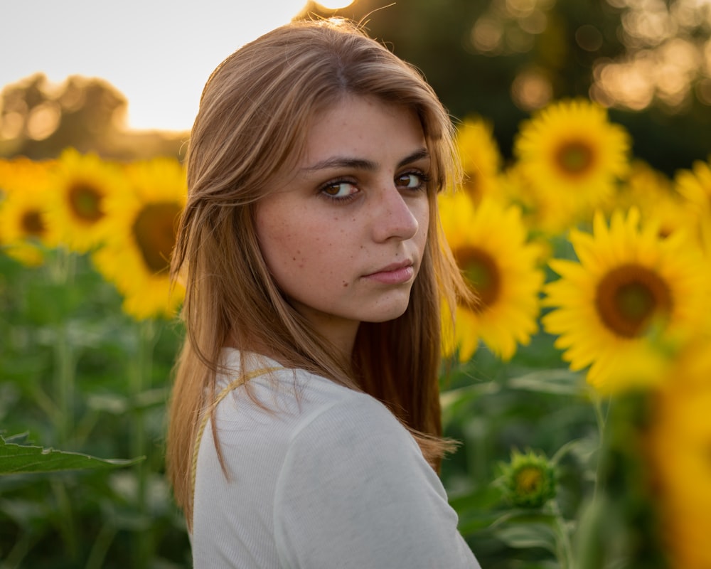 woman in white long sleeve shirt standing on sunflower field during daytime