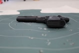 A handgun is placed on a shooting target with visible bullet holes and concentric circles. The focus is on the firearm lying flat on the target surface.