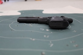 A handgun is placed on a shooting target with visible bullet holes and concentric circles. The focus is on the firearm lying flat on the target surface.