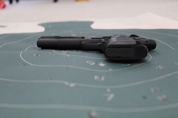 A handgun is placed on a shooting target with visible bullet holes and concentric circles. The focus is on the firearm lying flat on the target surface.