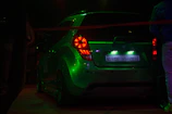 Close-up of a GTA 5 modded car with glowing neon green accents under city lights.