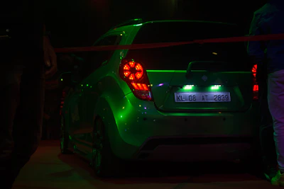 Close-up of a GTA 5 modded car with glowing neon green accents under city lights.