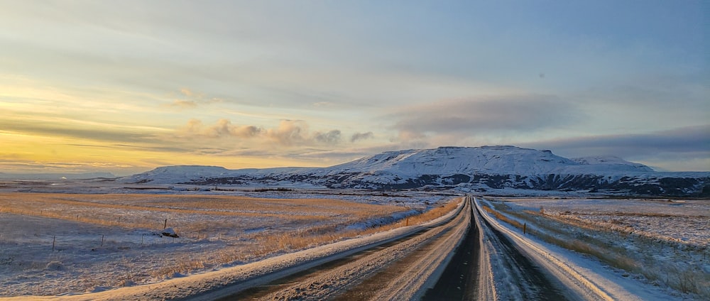 gray road in between snow covered field under white cloudy sky during daytime