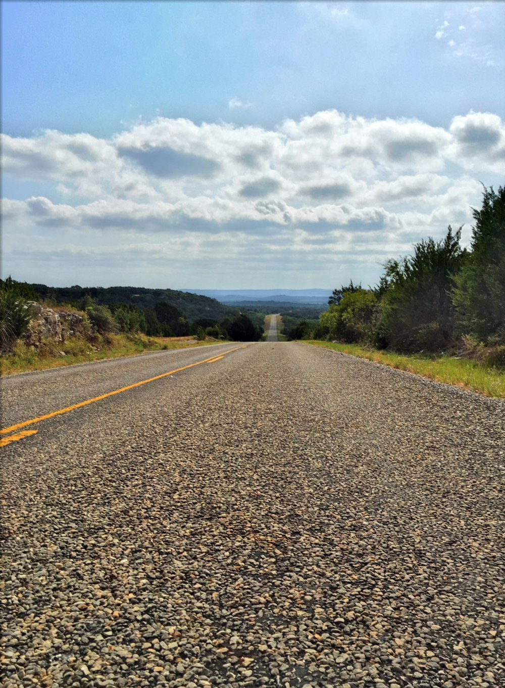 gray concrete road between green grass field under white clouds and blue sky during daytime